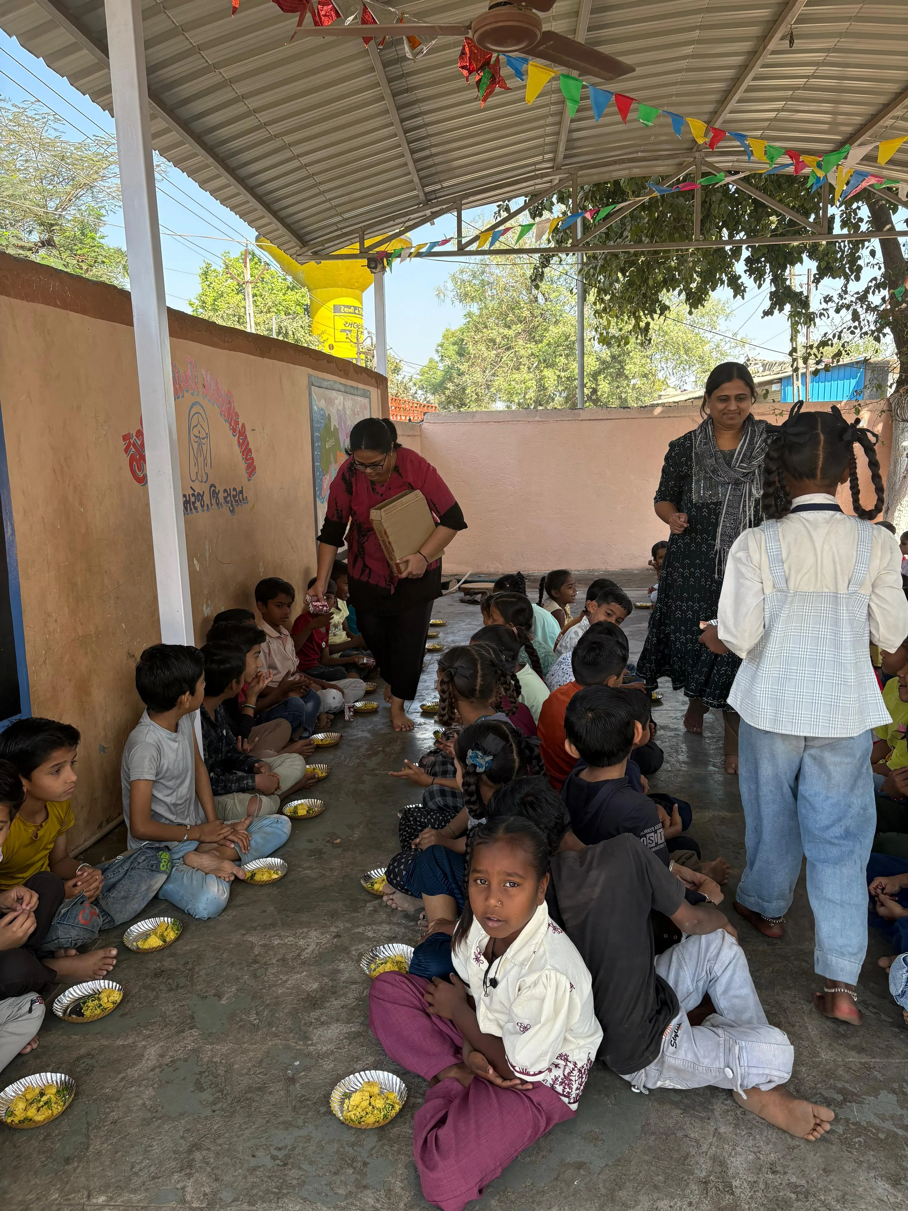 Yash Sharma and a volunteer serving children seated together during a community outreach event.